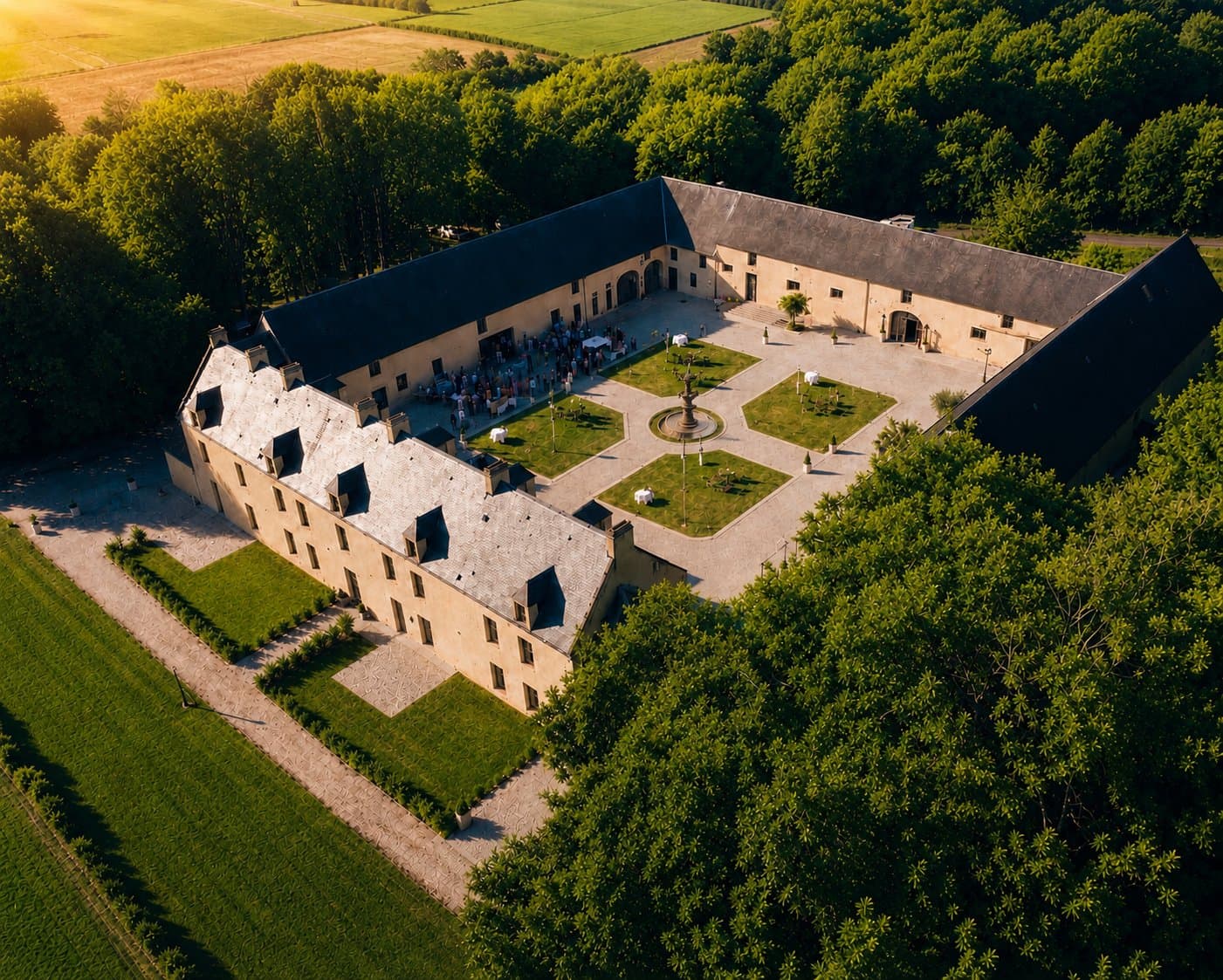 Vue aérienne du Domaine de la Cour des Lys à l'heure dorée — privatisation exclusive, Cour d'Honneur de 1500 m² avec la fontaine d'époque, cocktail en cours pour un mariage
