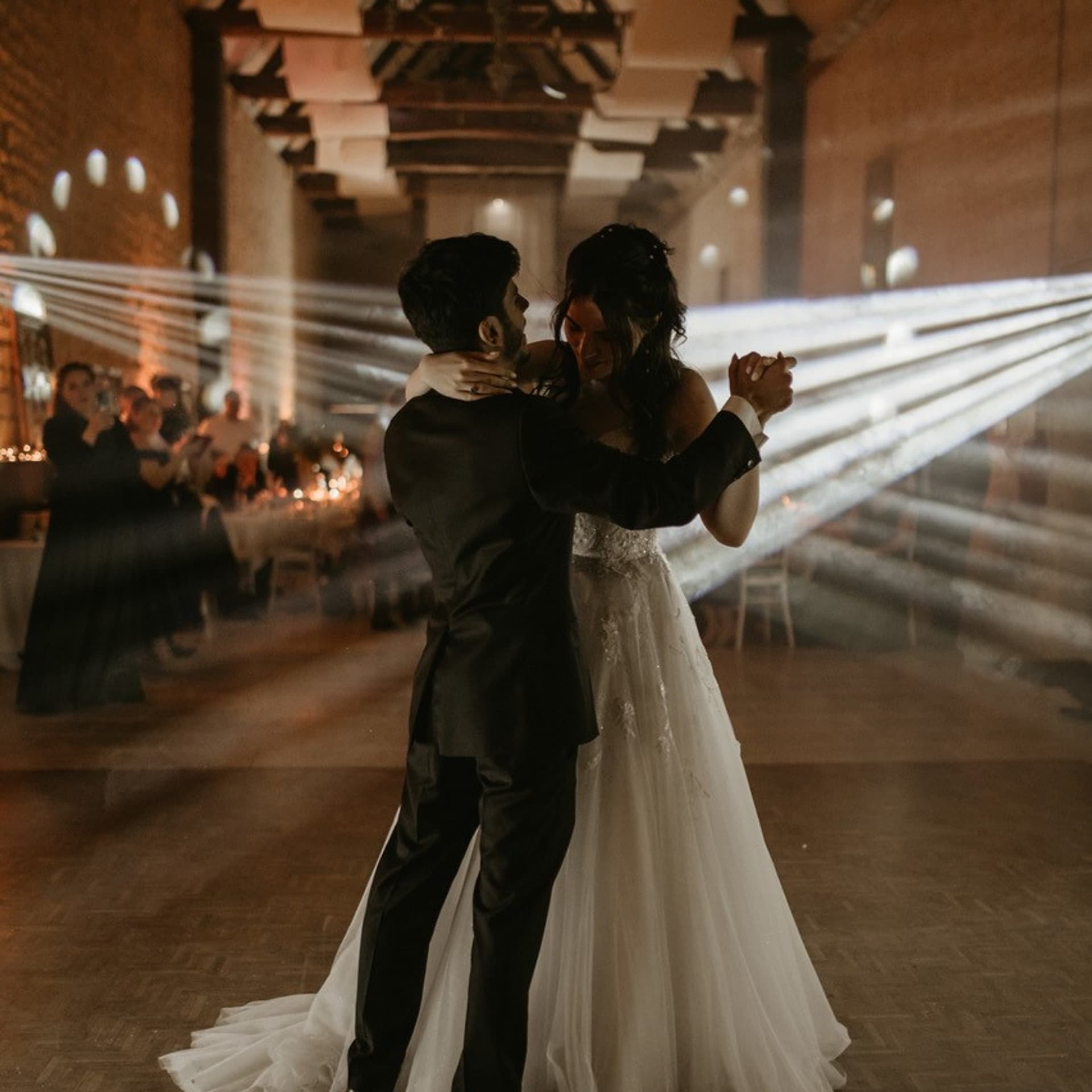 Mariés en pleine danse d'ouverture de bal sous les faisceaux lumineux, dans une salle du Domaine de la Cour des Lys