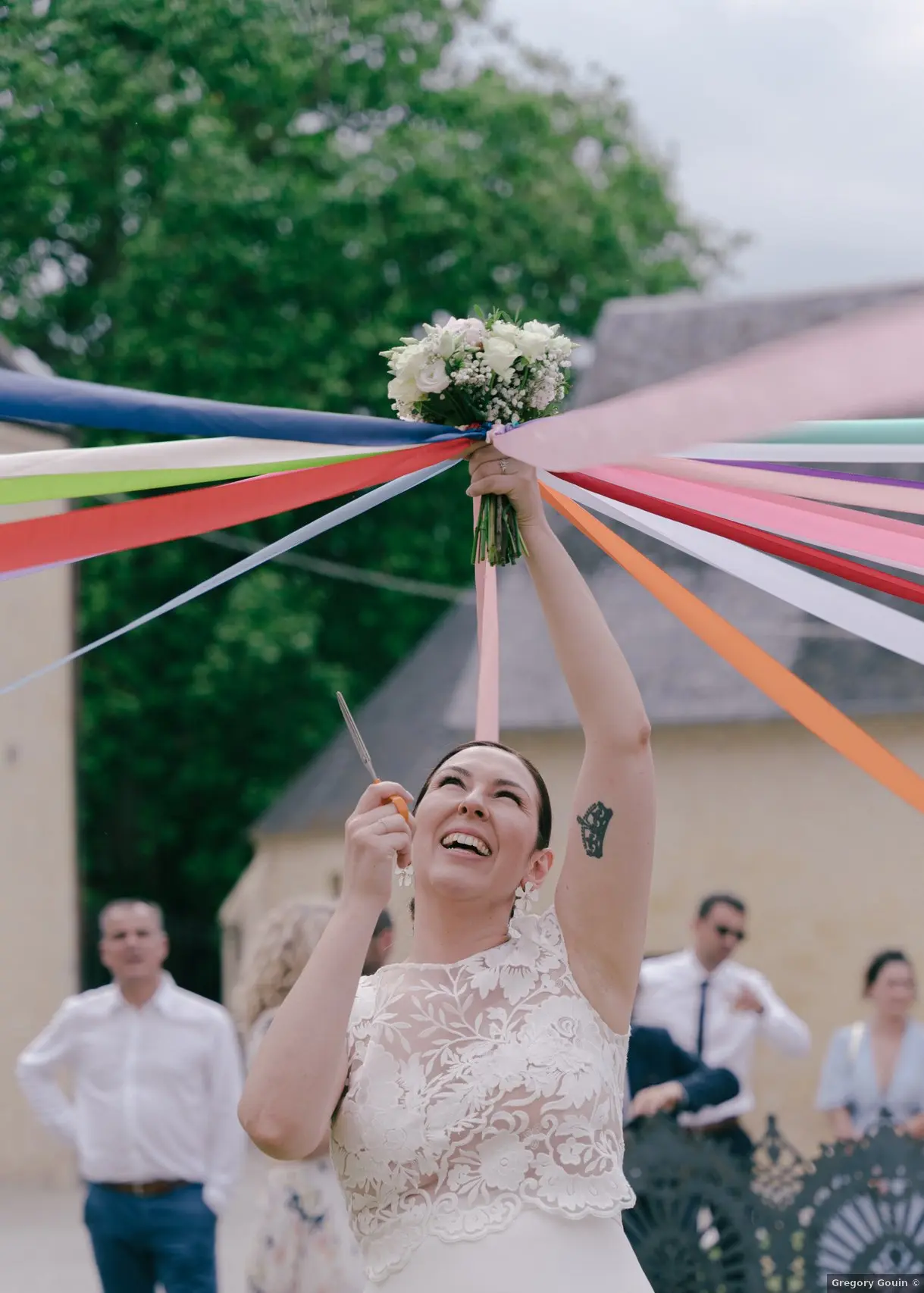 Cocktail mariage Cour d'Honneur Domaine de la Cour des Lys — Lise levant son bouquet entouré de rubans multicolores lors du jeu des rubans pendant le vin d'honneur