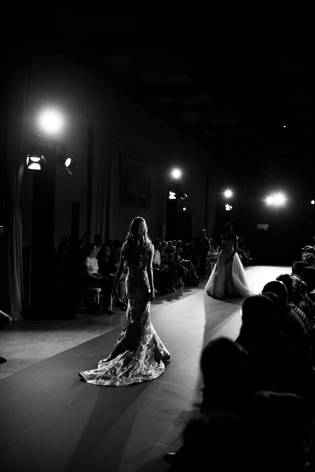Défilé du Festival de la Mode de Caen en noir et blanc — deux mannequins sur le podium sous les projecteurs, au Domaine de la Cour des Lys