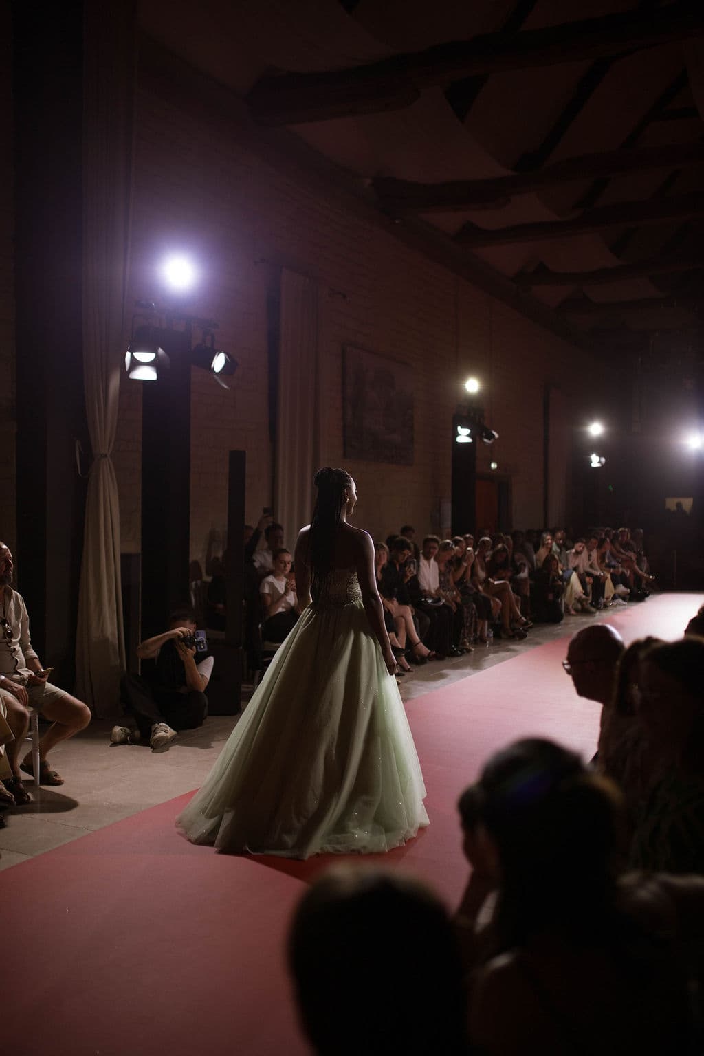 Mannequin en robe de tulle vert pâle sur le podium du défilé, sous les projecteurs, dans la salle du Domaine de la Cour des Lys — Festival de la Mode de Caen