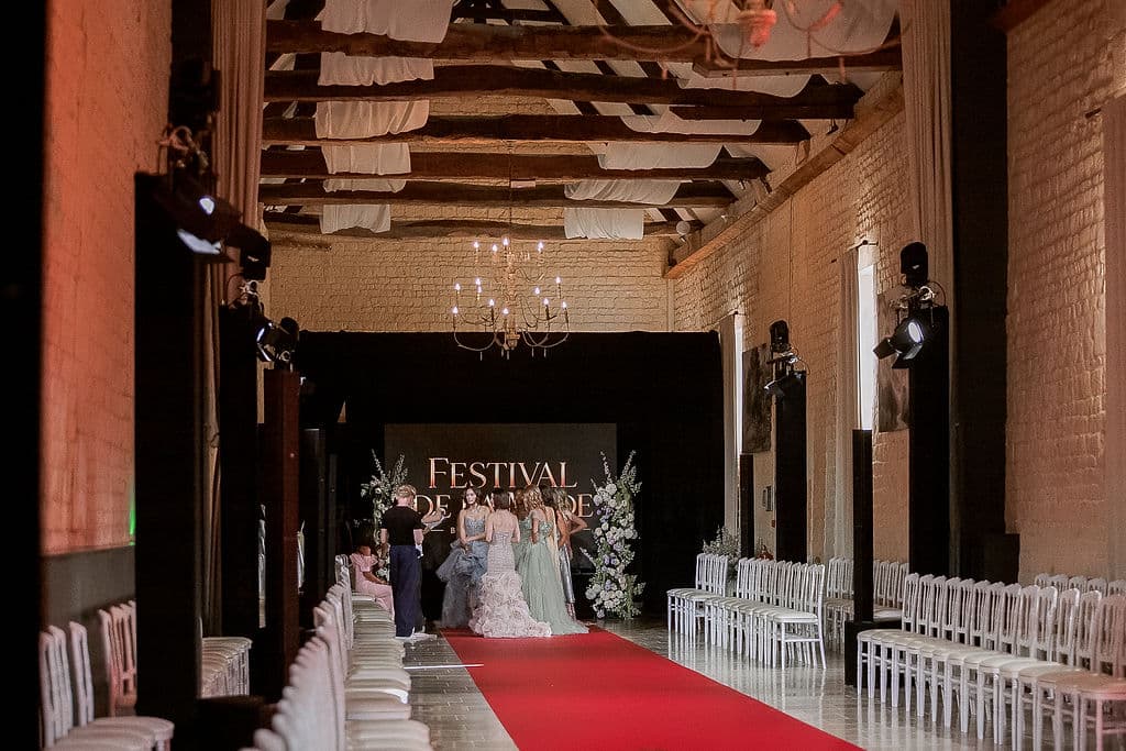 Podium du Festival de la Mode de Caen dressé dans la salle du Domaine de la Cour des Lys — tapis rouge, rangées de chaises, chandeliers et mannequins réunis devant le panneau du Festival