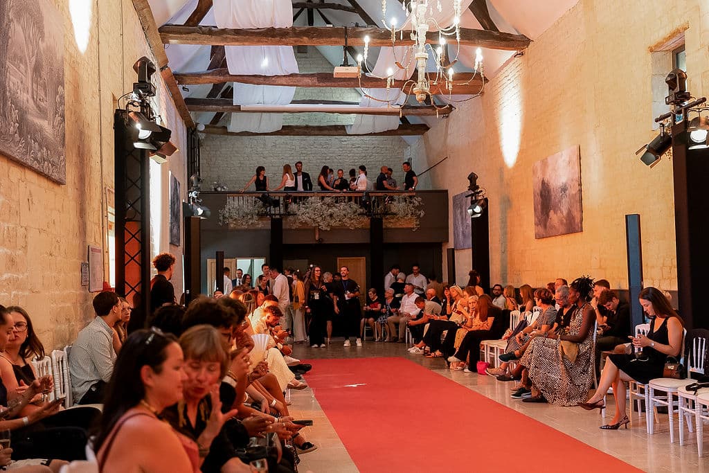 Grande salle du Domaine de la Cour des Lys transformée en salle de défilé — tapis rouge, poutres et chandeliers — lors du premier Festival de la Mode de Caen