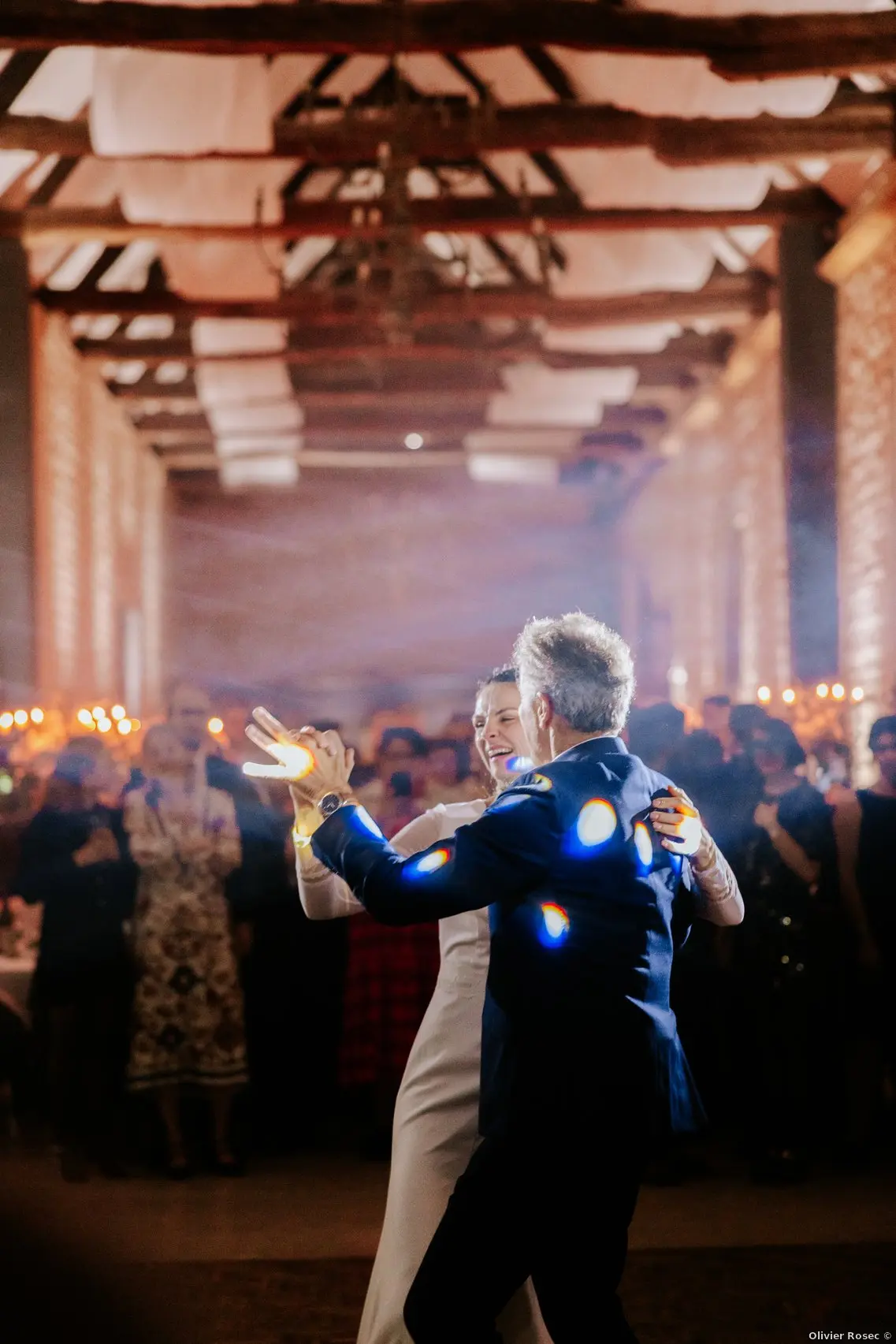 Soirée mariage salle Louis XVI Domaine de la Cour des Lys — mariée dansant, voilages blancs aux poutres anciennes, fumée et lumière chaude sur la piste