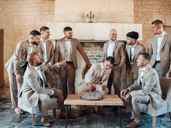 Baptiste et ses témoins en costumes beige sable et nœud papillon, dans une salle aux pierres apparentes — mariage au Domaine de la Cour des Lys