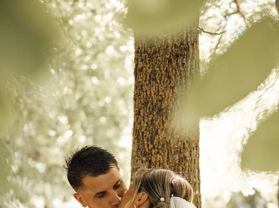 Baiser de Louise et Baptiste à contre-jour près d'un grand arbre — séance couple au Domaine de la Cour des Lys, juillet 2025